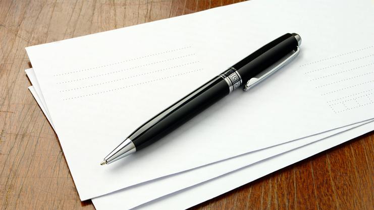 Schwarzer Kugelschreiber liegt auf einem Stapel weißer Blätter auf einer Holzoberfläche.